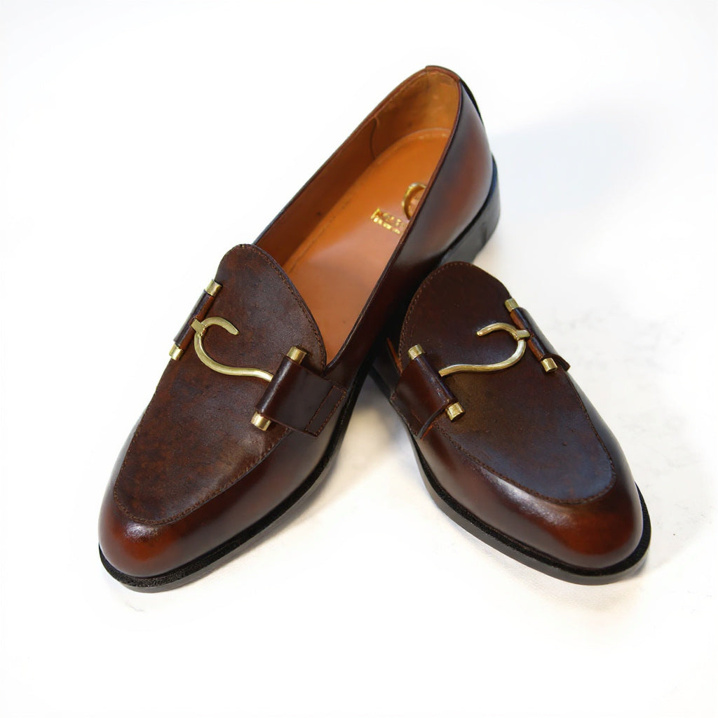 Pair of brown leather loafers with gold accents on a white background